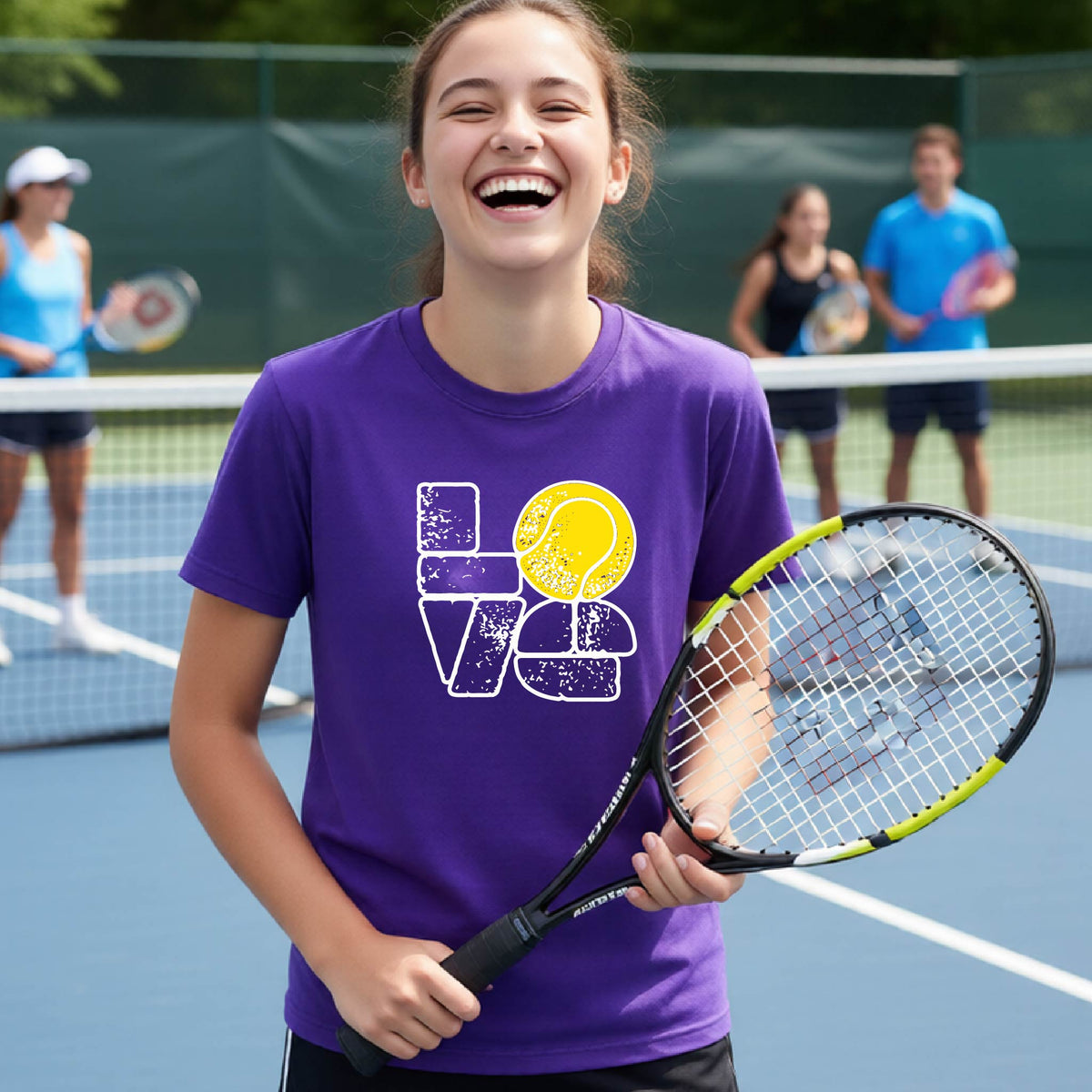 A smiling young tennis player stands on a blue court holding a tennis racket, wearing a purple graphic T-shirt with a distressed white 'LOVE' design and a yellow tennis ball motif. Two blurred players are visible in the background on the court.