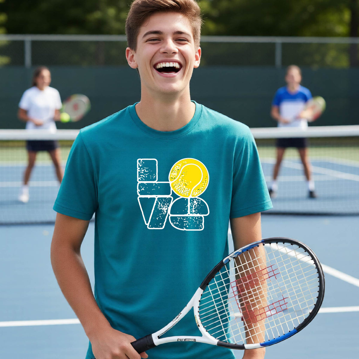A smiling young tennis player stands on a blue court holding a tennis racket, wearing a teal graphic T-shirt with a distressed white 'LOVE' design and a yellow tennis ball motif. Two blurred players are visible in the background on the court.