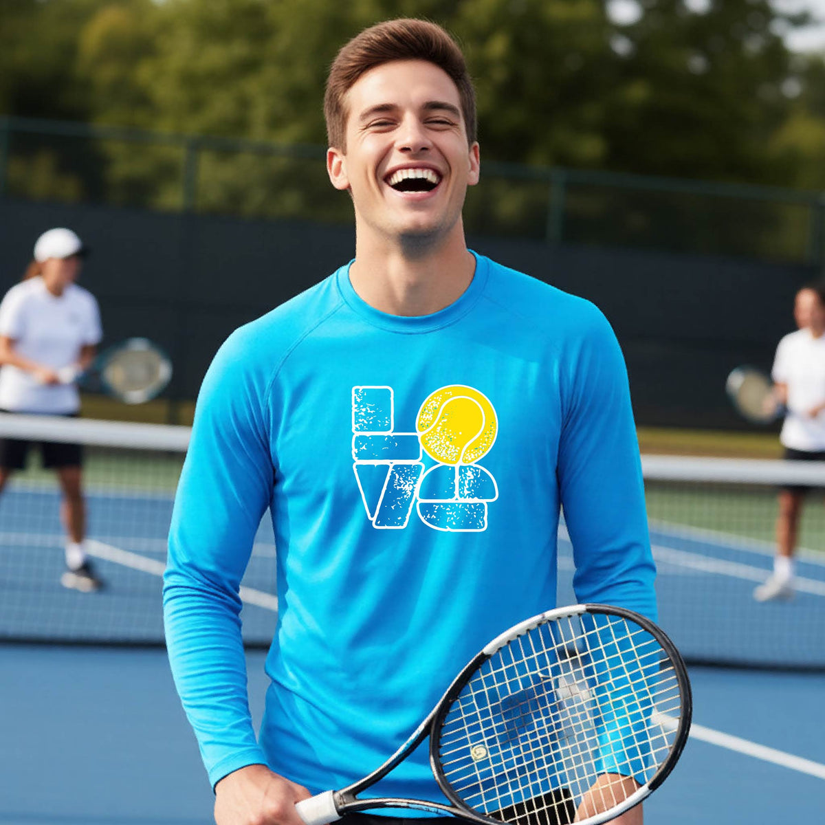 A man wearing a bright blue long-sleeve t-shirt with a white and yellow tennis-themed graphic "LOVE" with a tennis ball replacing the O, with a tennis  court and players in the background.