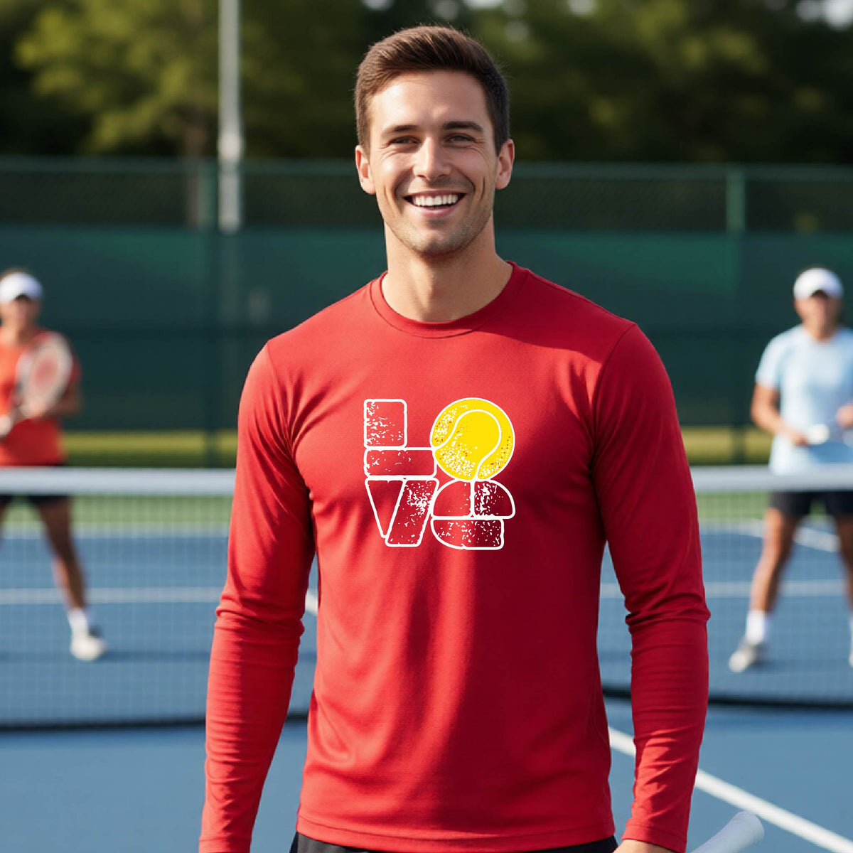 A man wearing a red long-sleeve t-shirt with a white and yellow tennis-themed graphic "LOVE" with a tennis ball replacing the O, with a tennis  court and players in the background.