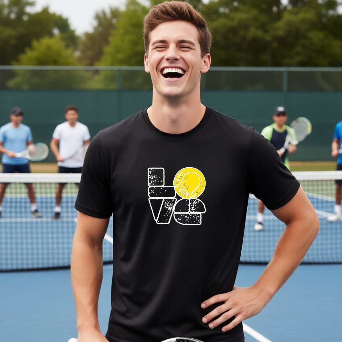 A man wearing a black short-sleeve t-shirt with a white and yellow tennis-themed graphic "LOVE" with a tennis ball replacing the O, with a tennis  court and players in the background.