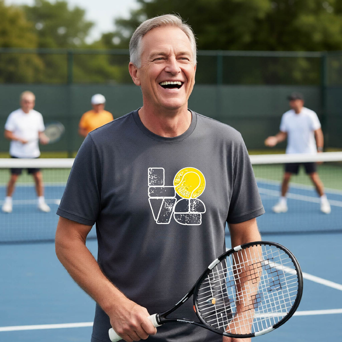 A man wearing a dark gray short-sleeve t-shirt with a white and yellow tennis-themed graphic "LOVE" with a tennis ball replacing the O, with a tennis  court and players in the background.