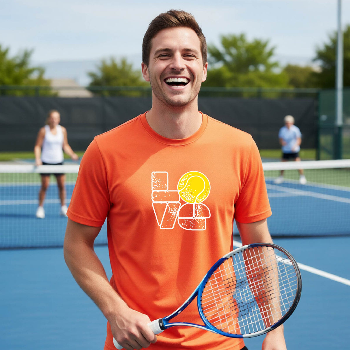 A man wearing an orange short-sleeve t-shirt with a white and yellow tennis-themed graphic "LOVE" with a tennis ball replacing the O, with a tennis  court and players in the background.