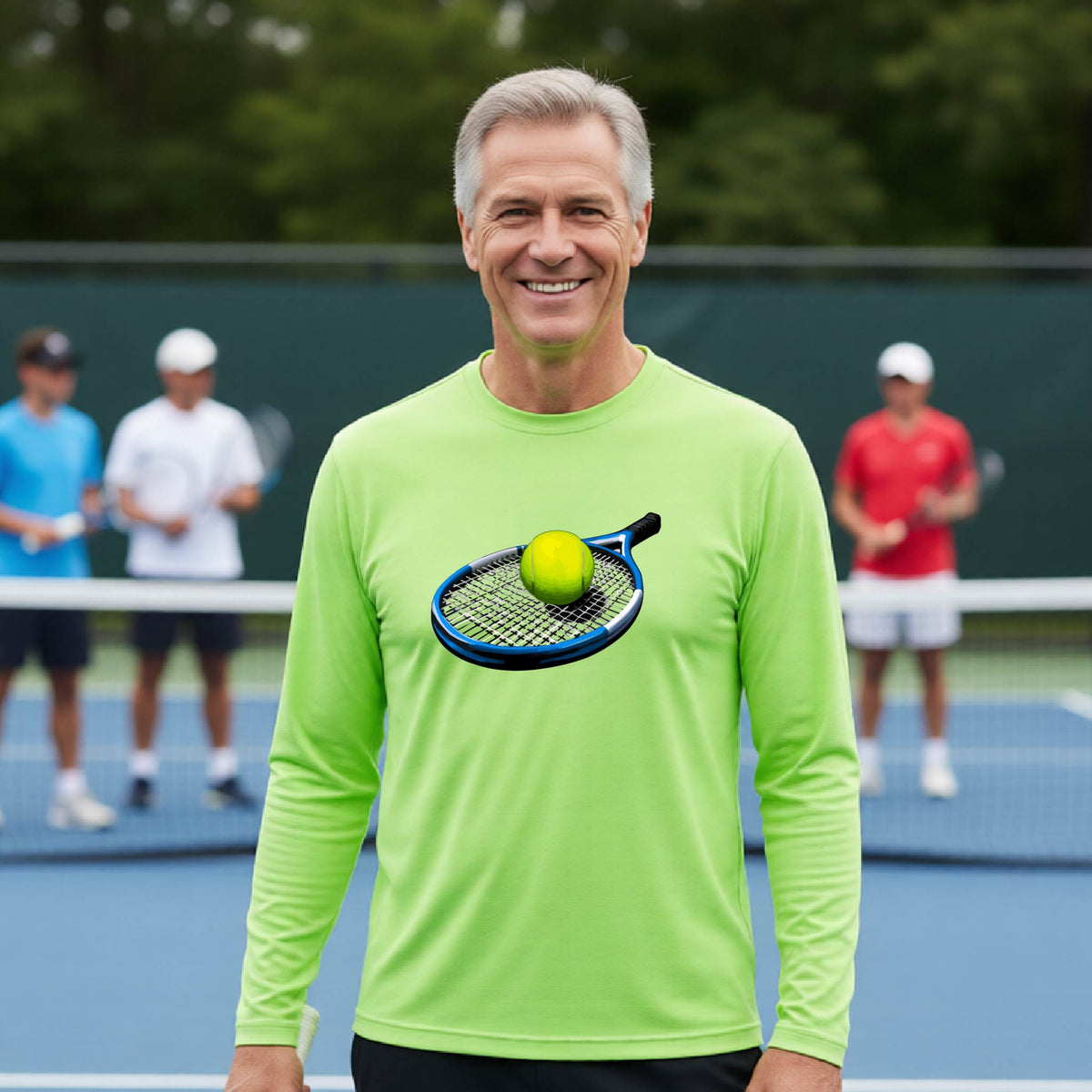 A smiling older man stands on a tennis court wearing a bright lime green long-sleeve shirt with a graphic of a tennis ball on a racket on the chest. Two other players are blurred in the background.