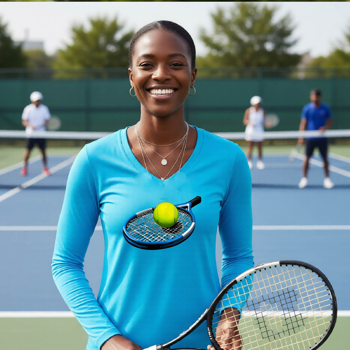 A smiling woman on a tennis court wearing a bright blue long-sleeve athletic shirt, holding a tennis racket, with a tennis ball resting on the racket. Two other players are visible in the background on the court.