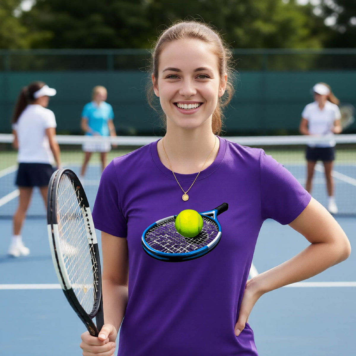 A smiling woman on a tennis court wearing a purple T-shirt with a graphic of a tennis racket and tennis ball on the chest, holding a tennis racket. Other players are blurred in the background.