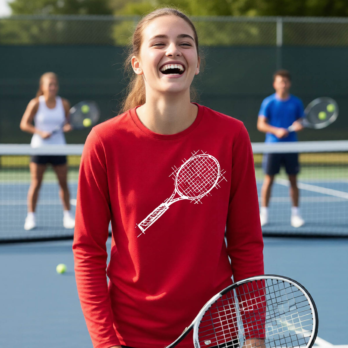 A young person on a blue tennis court holds a tennis racket and wears a red long-sleeve T-shirt with a white retro tennis racquet graphic.  