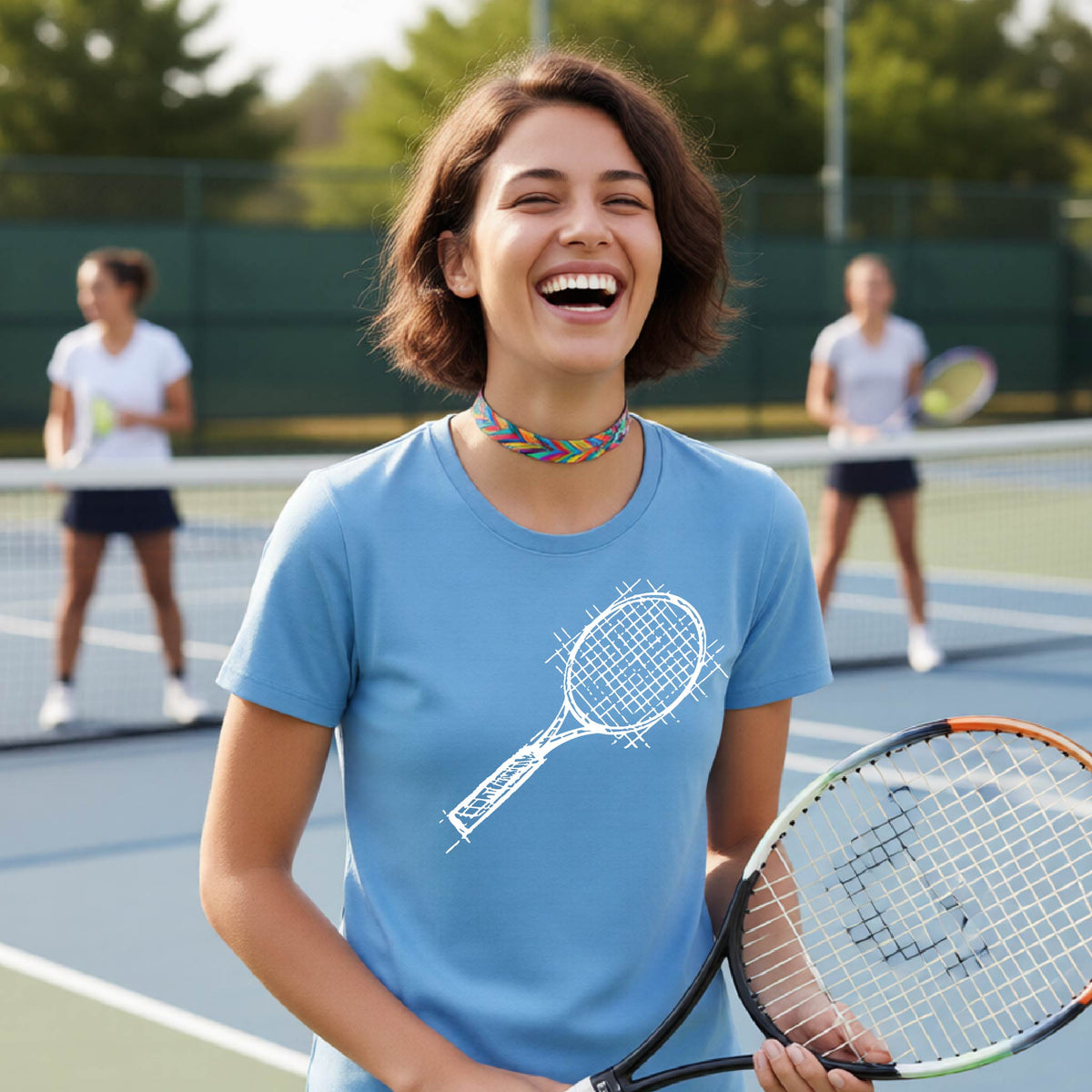 A woman on a blue tennis court holds a tennis racket and wears a blue short-sleeve T-shirt with a white retro tennis racquet graphic.  