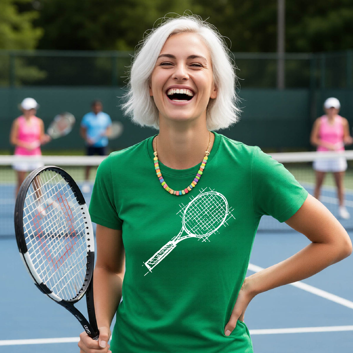 A woman on a blue tennis court holds a tennis racket and wears a green short-sleeve T-shirt with a white retro tennis racquet graphic.  
