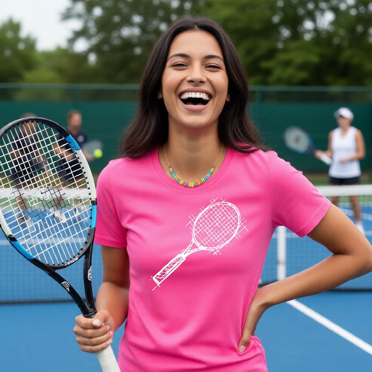 A woman on a blue tennis court holds a tennis racket and wears a pink short-sleeve T-shirt with a white retro tennis racquet graphic.  