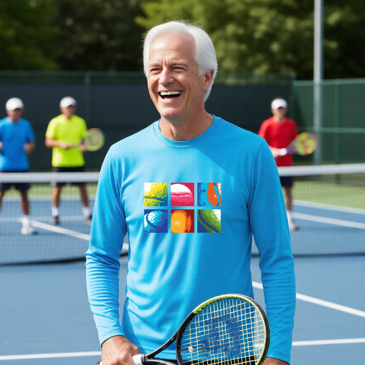 A smiling man on a blue tennis court holds a tennis racket and wears a bright blue long-sleeve T-shirt with a colorful 2x3 grid graphic on the chest of tennis balls. Other tennis players are blurred in the background.