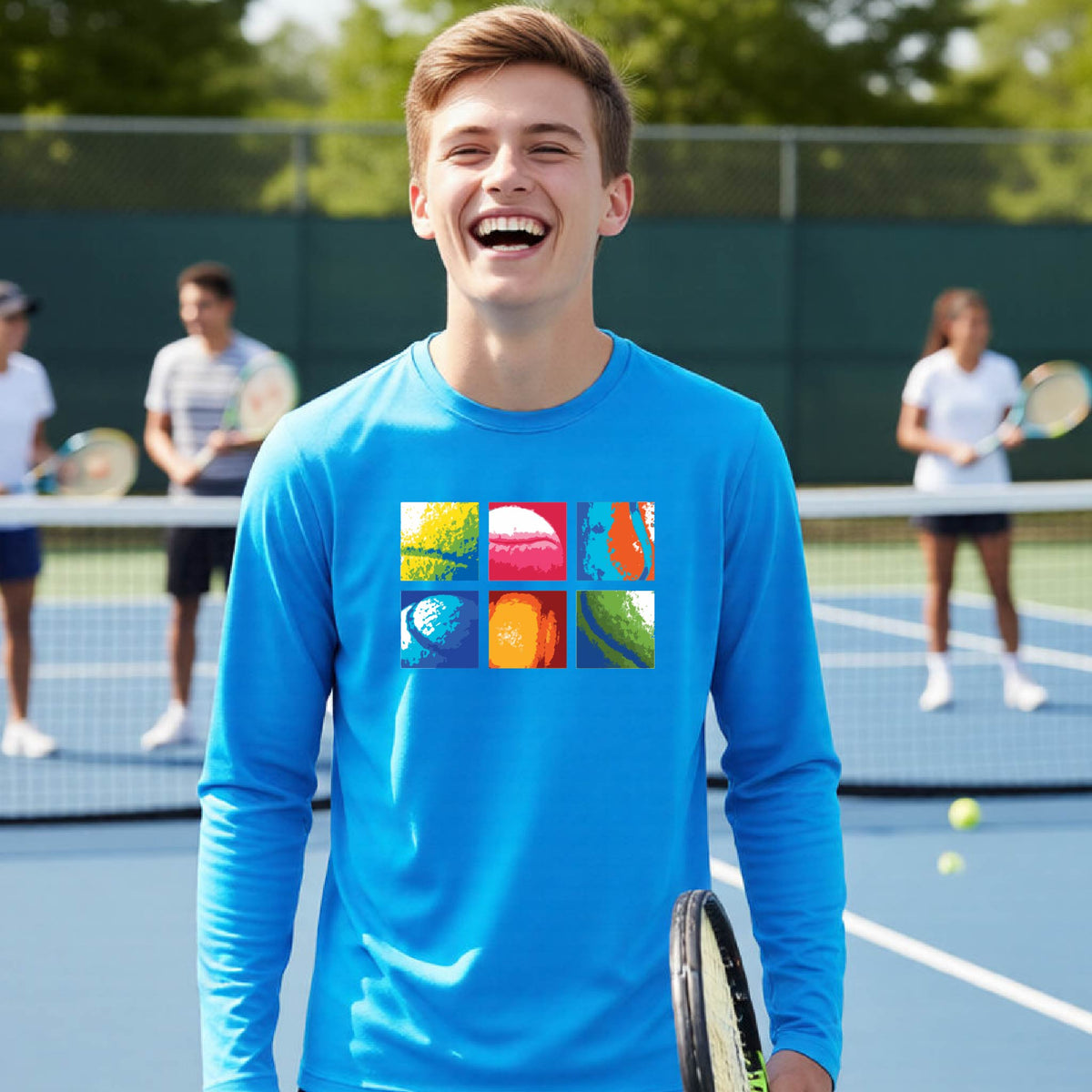 A young man smiling on a tennis court wearing a bright blue long-sleeve t-shirt with a colorful 2x3 graphic print of tennis balls and rackets on the chest.