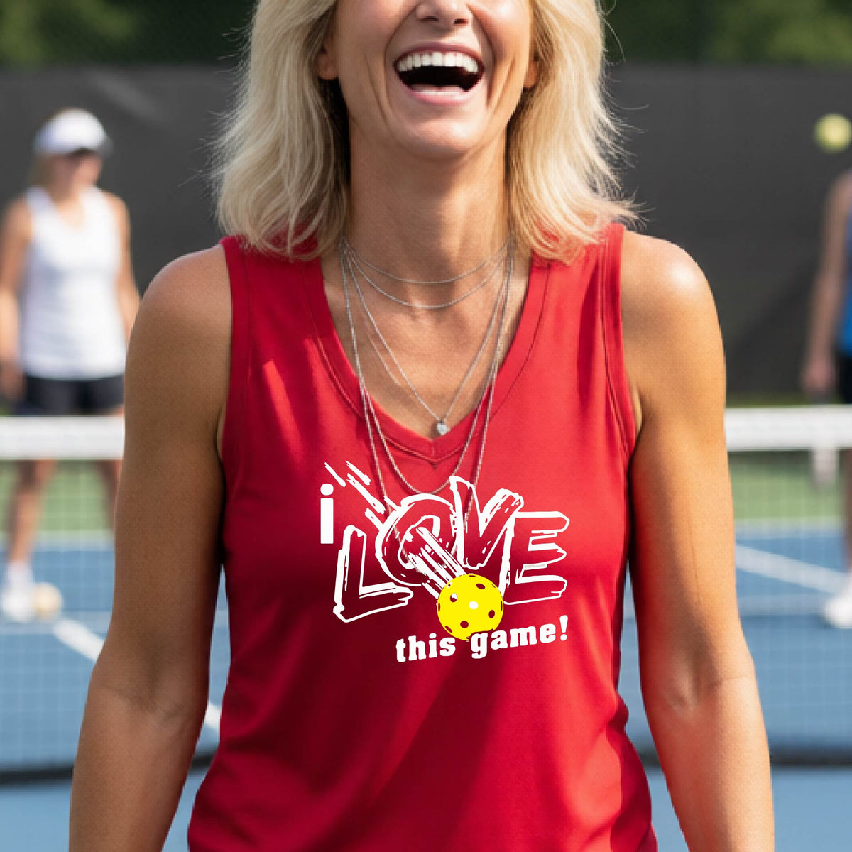 A woman on a pickleball court wearing a red sleeveless tank top with a white graphic that reads 'i LOVE this game!' and a yellow picklaball illustration.