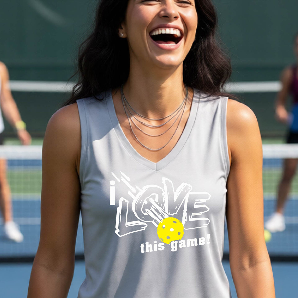 A woman on a pickleball court wearing a silver gray sleeveless tank top with a white graphic that reads 'i LOVE this game!' and a yellow picklaball illustration.