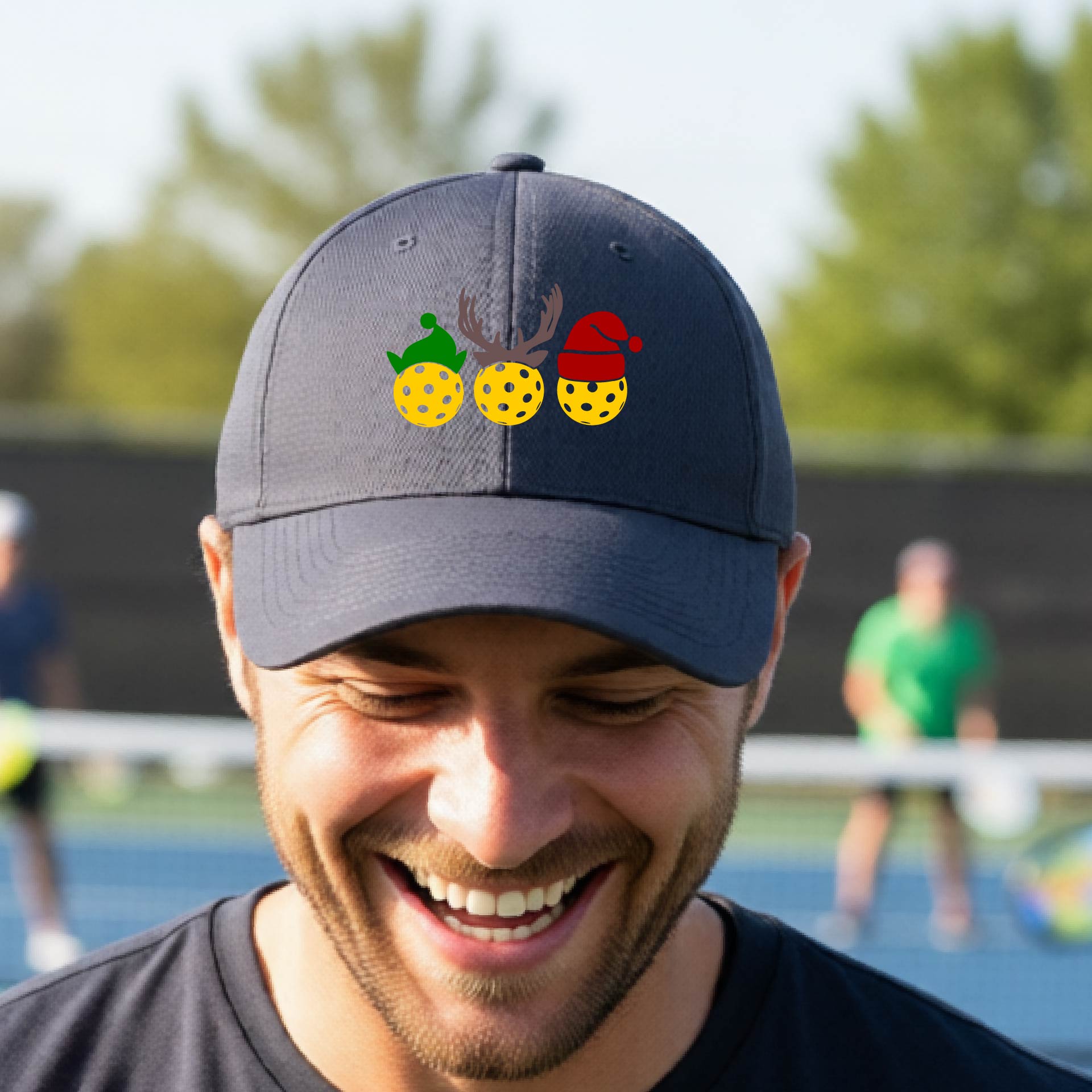 A graphite gray baseball hat with a pickleball Christmas graphic of three pickleballs wearing an elf hat, antlers and  santa hat.