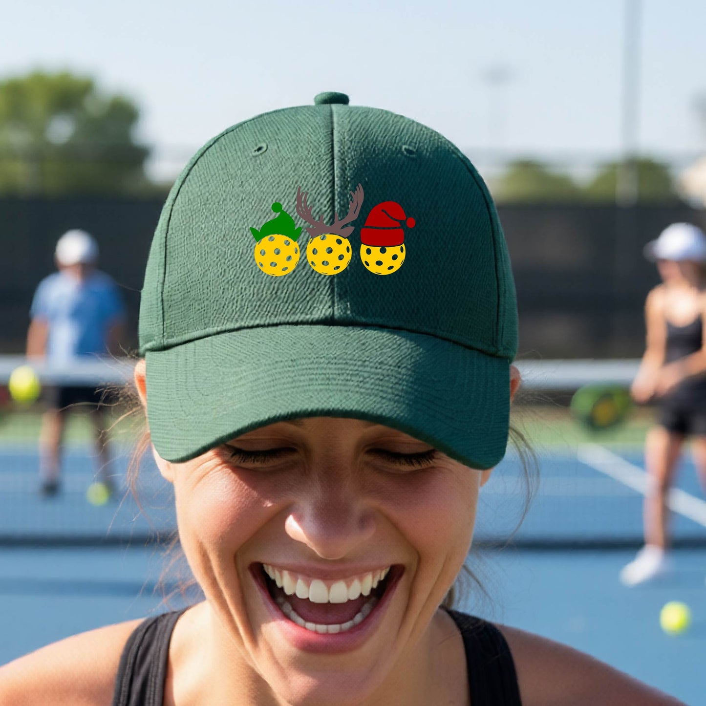 A green baseball hat with a pickleball Christmas graphic of three pickleballs wearing an elf hat, antlers and  santa hat.