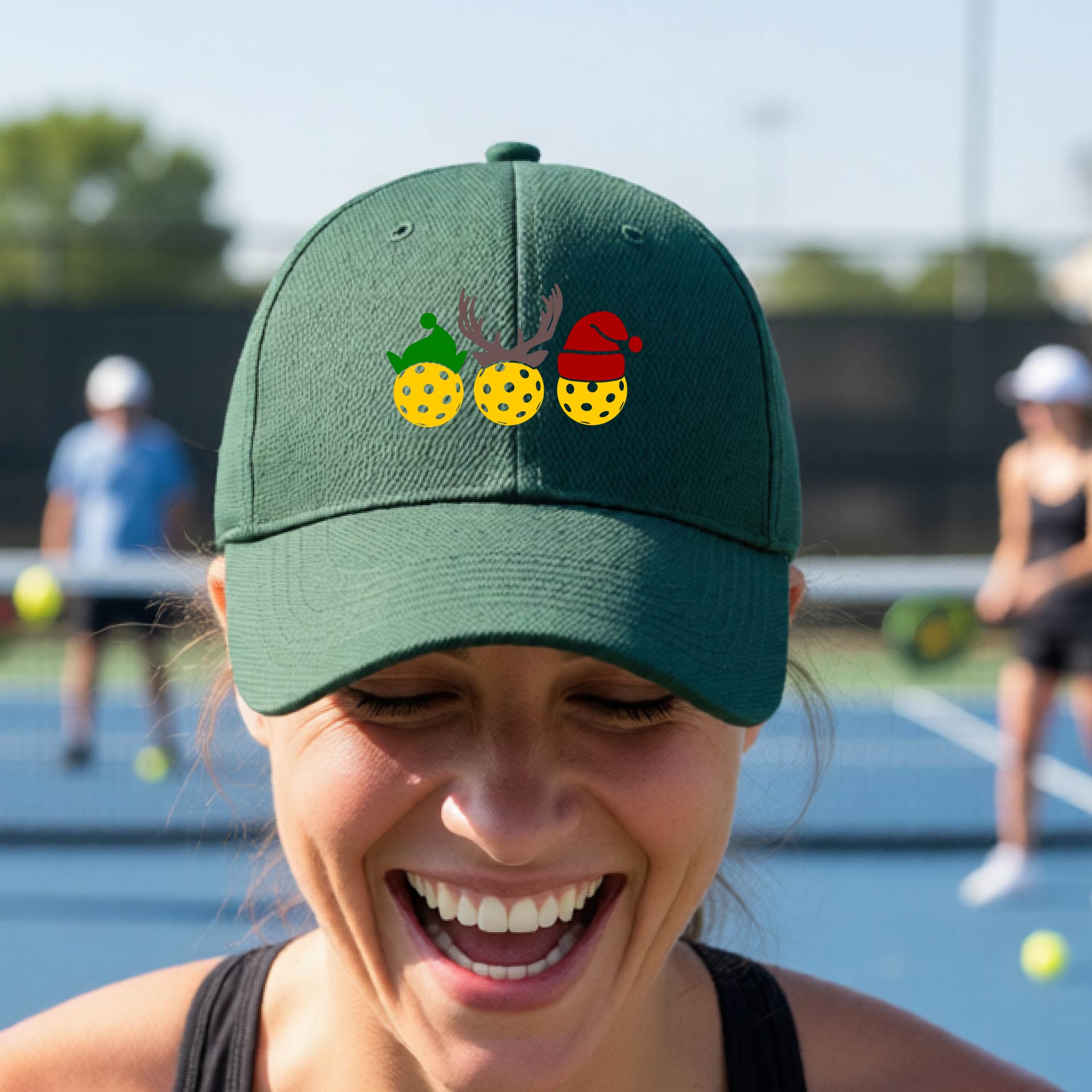 A green baseball hat with a pickleball Christmas graphic of three pickleballs wearing an elf hat, antlers and  santa hat.