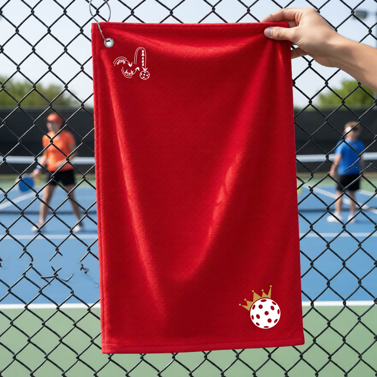 A close up of a red grommet and hook pickleball court towel with a DINK DINK SMASH graphic in the upper left corner and a white pickleball crown with ball graphic in the bottom right corner. 