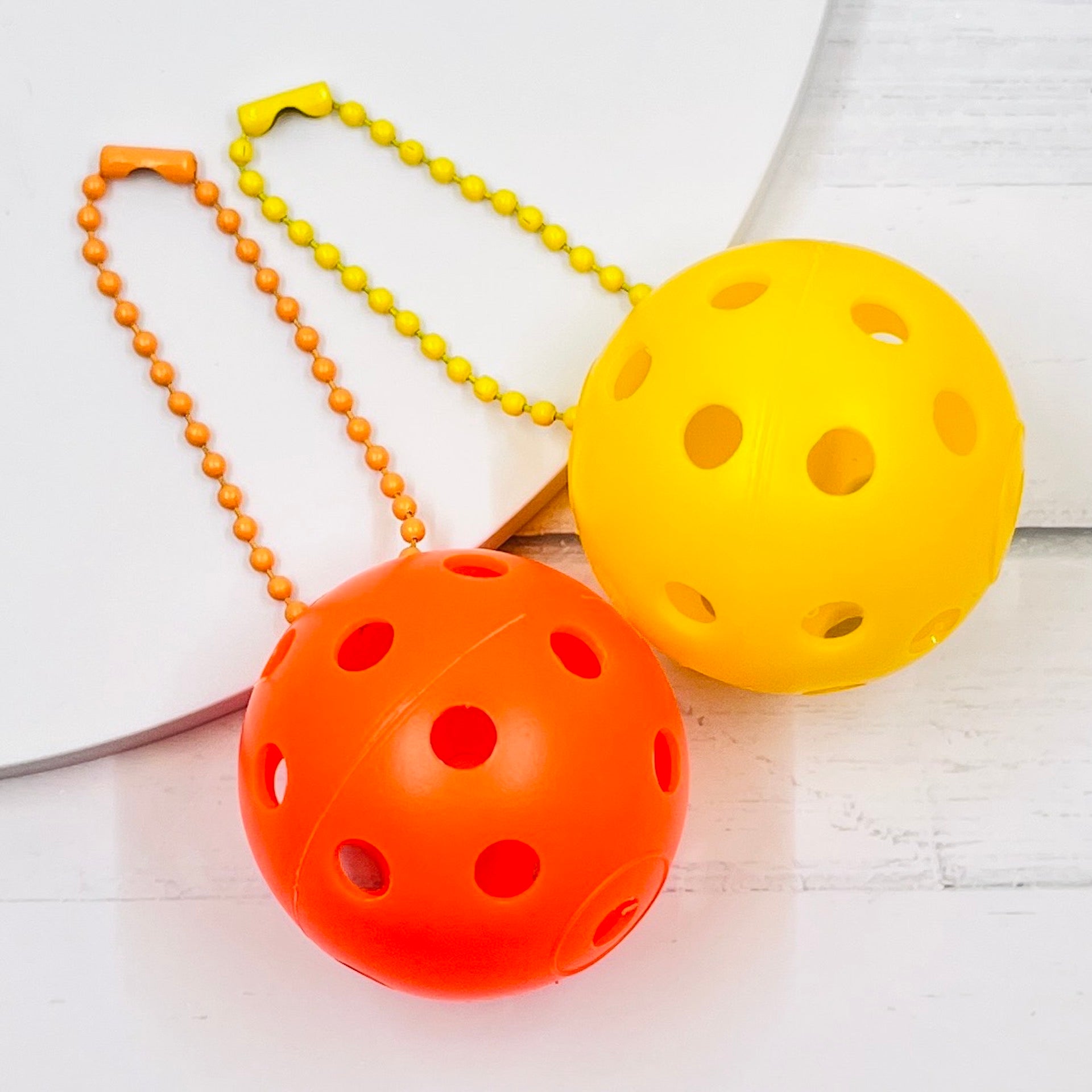 Mini Pickleball Bag Tags/Pulls (Set of 2)  Each order gets you 2 of the little mini pickleballs and chain! They measure about 1 1/2 inches and are used as bag tag markers. Fun for any bag, especially your pickleball bag!! The balls come in 7 colors: Red, Green, Blue, Orange, White, Pink, and Yellow. Choose 2 of the 7 fun colors.