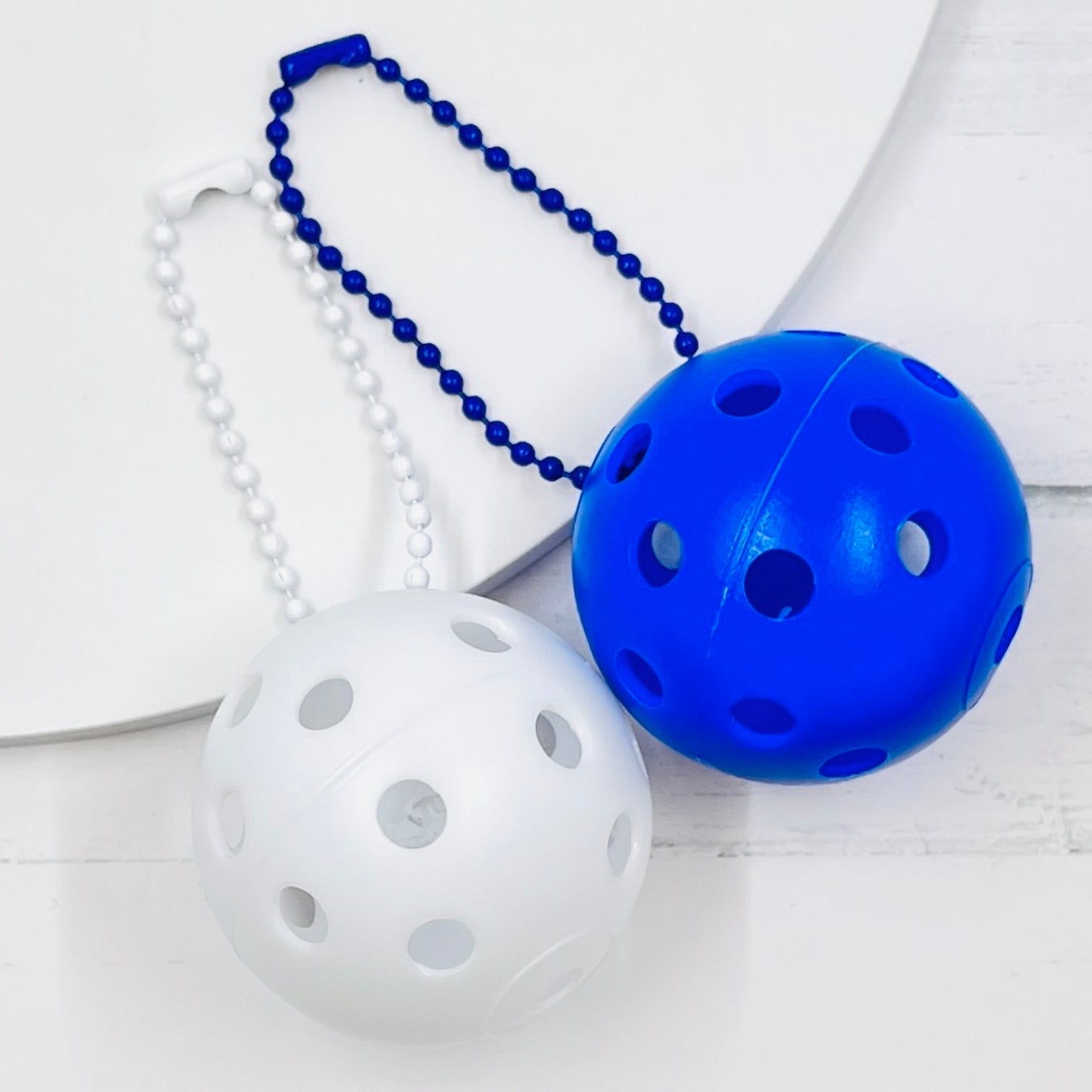 Mini Pickleball Bag Tags/Pulls (Set of 2)  Each order gets you 2 of the little mini pickleballs and chain! They measure about 1 1/2 inches and are used as bag tag markers. Fun for any bag, especially your pickleball bag!! The balls come in 7 colors: Red, Green, Blue, Orange, White, Pink, and Yellow. Choose 2 of the 7 fun colors.