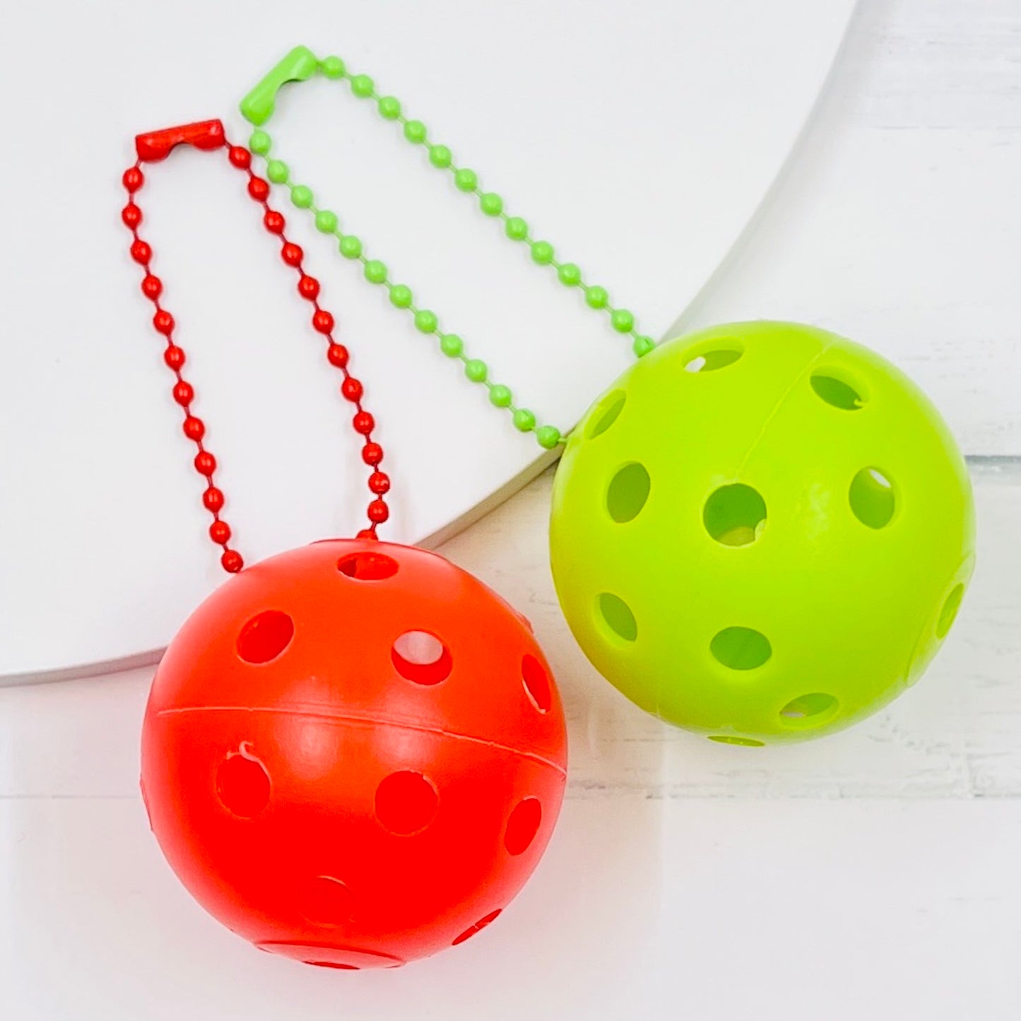 Mini Pickleball Bag Tags/Pulls (Set of 2)  Each order gets you 2 of the little mini pickleballs and chain! They measure about 1 1/2 inches and are used as bag tag markers. Fun for any bag, especially your pickleball bag!! The balls come in 7 colors: Red, Green, Blue, Orange, White, Pink, and Yellow. Choose 2 of the 7 fun colors.