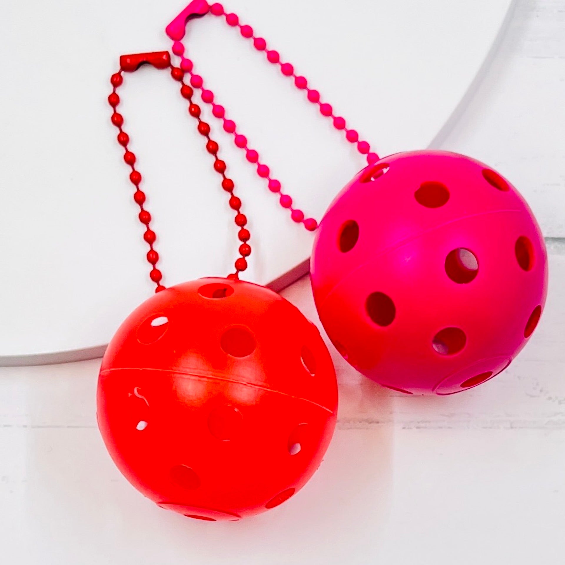 Mini Pickleball Bag Tags/Pulls (Set of 2)  Each order gets you 2 of the little mini pickleballs and chain! They measure about 1 1/2 inches and are used as bag tag markers. Fun for any bag, especially your pickleball bag!! The balls come in 7 colors: Red, Green, Blue, Orange, White, Pink, and Yellow. Choose 2 of the 7 fun colors.