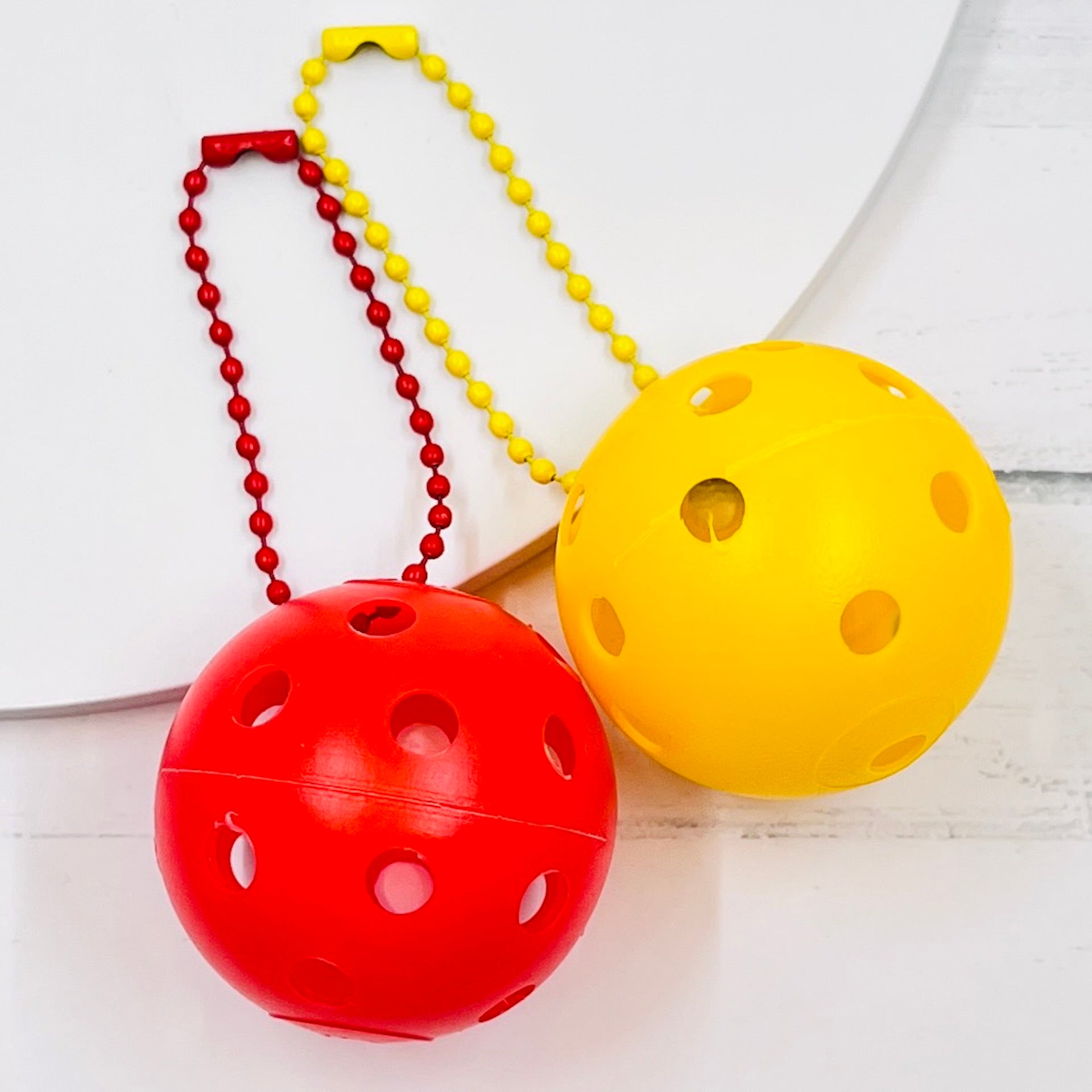 Mini Pickleball Bag Tags/Pulls (Set of 2)  Each order gets you 2 of the little mini pickleballs and chain! They measure about 1 1/2 inches and are used as bag tag markers. Fun for any bag, especially your pickleball bag!! The balls come in 7 colors: Red, Green, Blue, Orange, White, Pink, and Yellow. Choose 2 of the 7 fun colors.