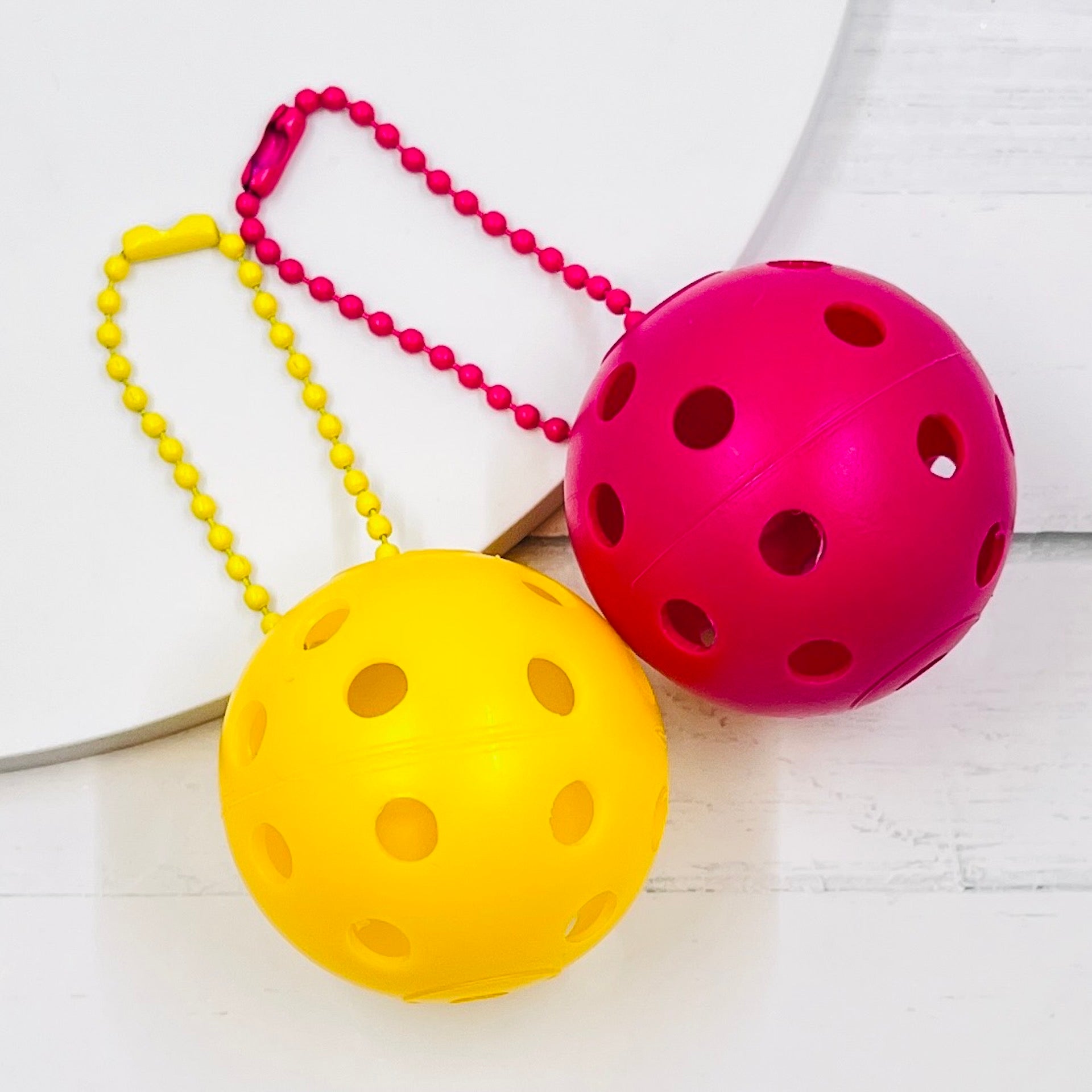 Mini Pickleball Bag Tags/Pulls (Set of 2)  Each order gets you 2 of the little mini pickleballs and chain! They measure about 1 1/2 inches and are used as bag tag markers. Fun for any bag, especially your pickleball bag!! The balls come in 7 colors: Red, Green, Blue, Orange, White, Pink, and Yellow. Choose 2 of the 7 fun colors.