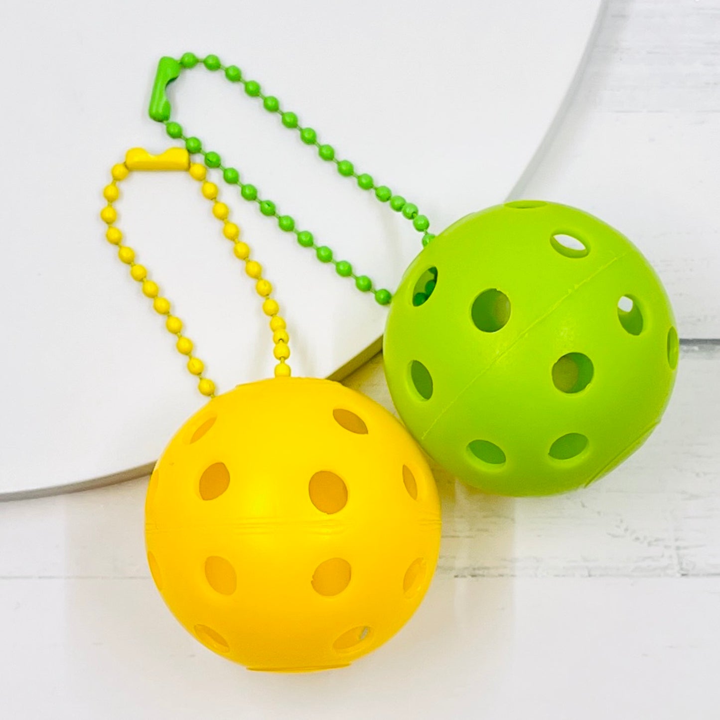 Mini Pickleball Bag Tags/Pulls (Set of 2)  Each order gets you 2 of the little mini pickleballs and chain! They measure about 1 1/2 inches and are used as bag tag markers. Fun for any bag, especially your pickleball bag!! The balls come in 7 colors: Red, Green, Blue, Orange, White, Pink, and Yellow. Choose 2 of the 7 fun colors.