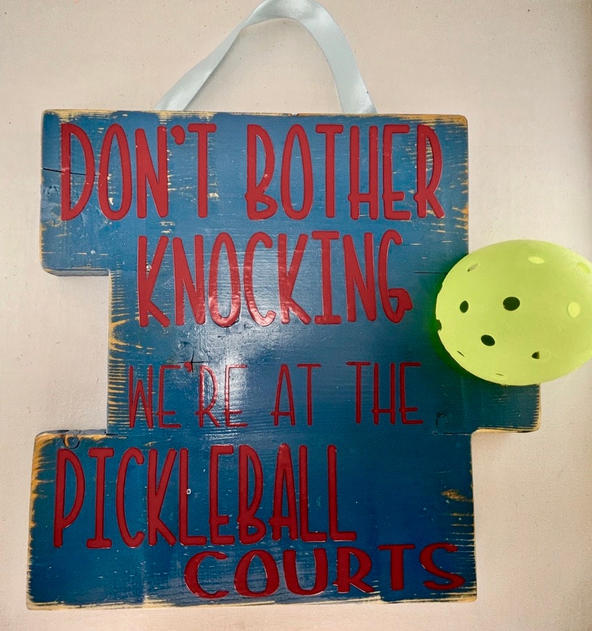 We're at the Pickleball Courts - Home Decor Door Decorations  Decorate your porch with this funny and super fun Pickleball sign. This sign uses an upcycled pickleball! It also comes in a "vintage" style. You get to customize the color of sign and the color of words you want to help match any home design.